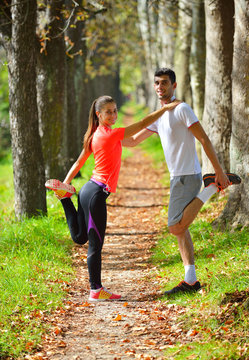 Young couple stretching legs before running in autumn nature