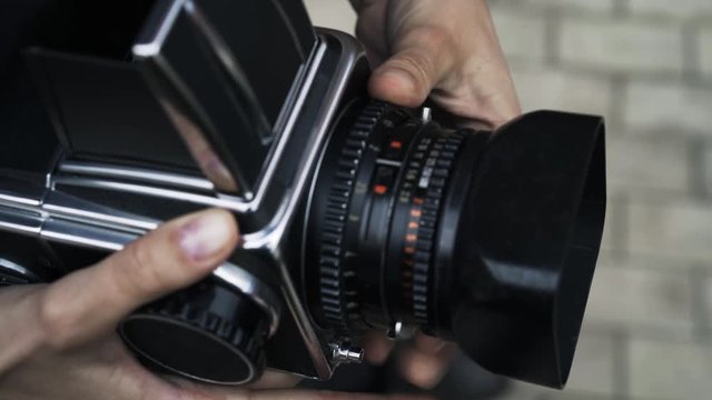 Close up of hands of a young woman adjusting an old fashioned camera. She has long tan fingers. Tilt up real time close up shot