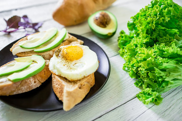 Tasty sandwiches with avocado and egg on plate on white wooden table. Delicious breakfast