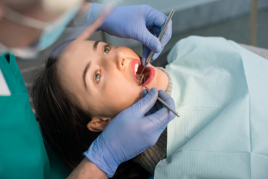 Close up of beautiful young woman having dental check up in dental clinic. Dentist examining a patient's teeth with dental tools - mirror and probe. Dentistry.
