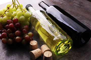Bottle of white and red wine, grape and corks on wooden table