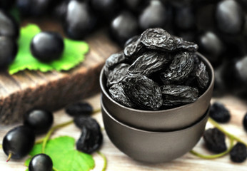 Dried black raisins in bowl with fresh ripe grapes