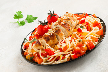 Pasta and fresh vegetable salad and grilled chicken breasts on the black plate.