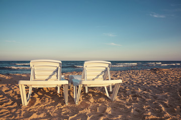 Two deckchairs on the beach with bright sun and waves