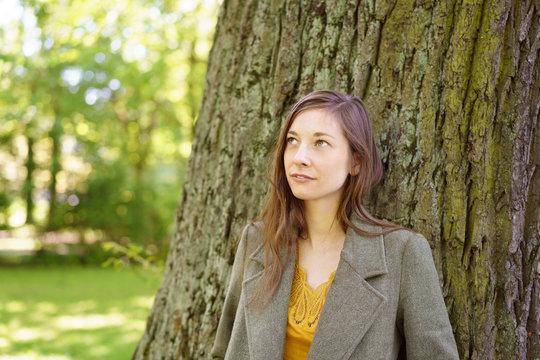 Thoughtful sad young woman leaning on a tree