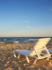 Deckchairs on the beach with bright sun and waves
