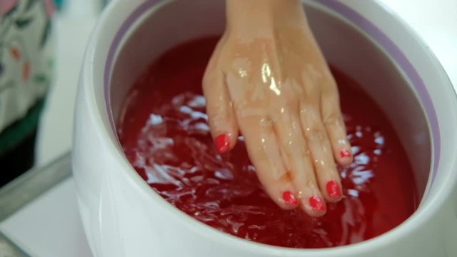 Woman puts his hand in a tray with a red paraffin several times. In the beauty salon there is paraffin therapy, this is a special heat compress, during which a molten mixture is used. Material has