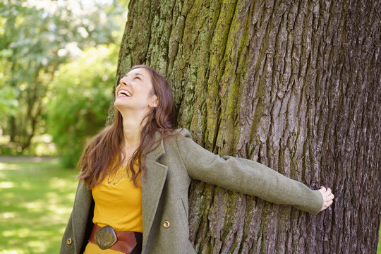 Cheerful young woman embracing tree