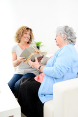 mature woman offering present gift to elderly senior lady for mother's day or birthday anniversary