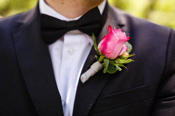 man in a gray suit corrects hand of a red rose boutonniere