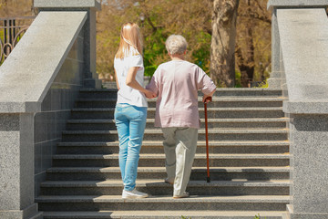 Elderly woman and young caregiver in park on sunny day