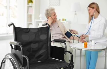 Wheelchair and blurred young nurse measuring blood pressure of elderly woman on background