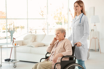 Obraz premium Young nurse and disabled elderly woman in wheelchair at home