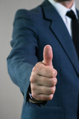 Young businessman man in jacket and white shirt shows gesture approval, thumb up. Business concept, focus on hand
