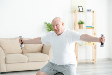Fat senior man training with dumbbells at home. Weight loss concept