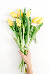 Female hand holding beautiful yellow tulip flowers bouquet on white background. Flat lay, top view.