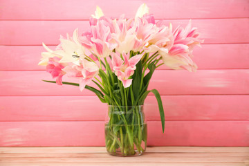 Glass vase with beautiful tulips on color wooden background