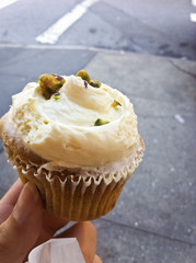 Cupcake mit Pistazien in der Hand mit Straße im Hintergrund