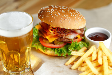 Big tasty burger and fries with beer on foreground on the wooden table