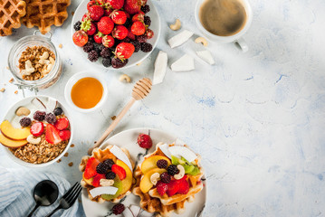 Breakfast. Home-made fresh Belgian soft wafers with honey, fresh fruits, nuts and berries; Yoghurt with granola and fruit, a cup of coffee. Light concrete table. Copy space   top view
