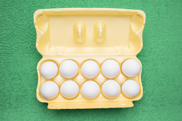 Ten white chicken eggs in a yellow tray lie on a grassy-green background
