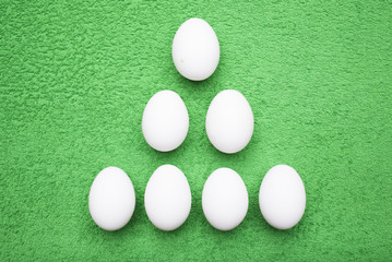 White chicken eggs lie in the form of a triangle on a juicy grassy-green background