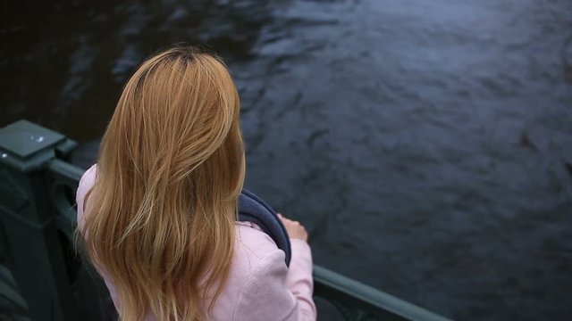 A woman in a coat stands on a bridge and looks down at the black water. She wants to commit suicide