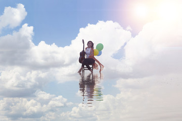 Girl playing guitar while sitting on the chair. Sea reflection and colorful balloons 