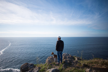 Tall young man in urban casual clothing, stands on edge of mountain and overlooks ocean views on...