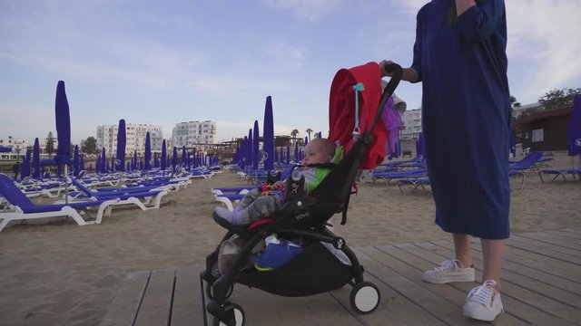 Beautiful woman pushes baby carriage with her son. Family vacations at seaside resort. Camera follows the lady, handheld shot