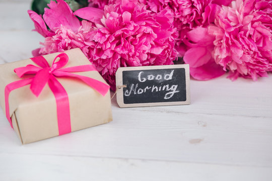 Pink peony flowers,gift box and notes good morning on white rustic table from above, breakfast on Mothers day or Womens day .