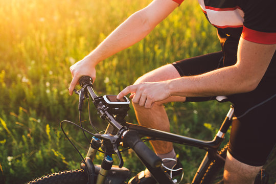 A young brunette guy on a mountain bike uses a cycling computer, a navigator in the field sunset of the day