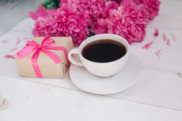 A cup of coffee, pink peonies pattern and gift box on wooden background