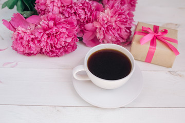 A cup of coffee, pink peonies pattern and gift box on wooden background
