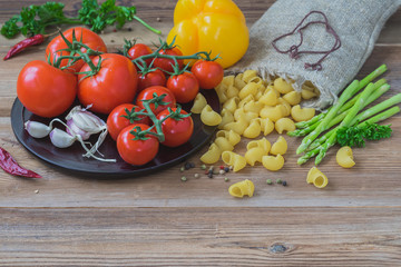 Italian food cooking ingredients on wooden background, dry pasta, vegetables, fresh tomatoes, asparagus, bell pepper. Concept of vegetarian, healthy food, copy space