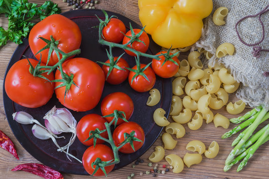 Ingredients for italian food - uncooked Italian pasta and vegetables, different varieties of tomatoes, garlic, asparagus, bell pepper on wooden background. Top view