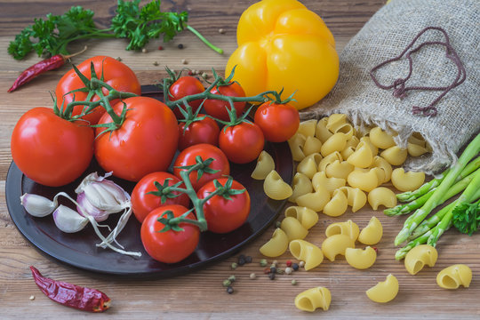 Ingredients for traditional italian cuisine - dry pasta, vegetables, fresh tomatoes, garlic, asparagus, yellow bell pepper. Concept vegetarian, healthy food. Top view