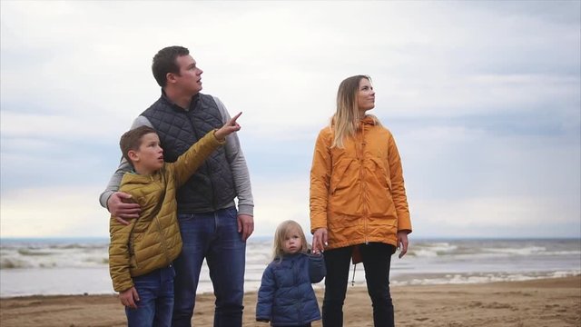 A young son is pointing at a certain object, his father explains what is there, his wife and his little son are enjoying a holiday together near the sea