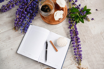 A Cup of coffee,note book , cracker, cookie, biscuit, lupins flowers on a wooden table.