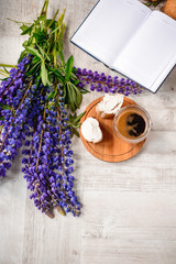 A Cup of coffee,note book , cracker, cookie, biscuit, lupins flowers on a wooden table.