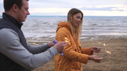 A young mother, her adult husband and their son lit the Bengal lights near the sea, a happy family is standing on the beach in warm clothes