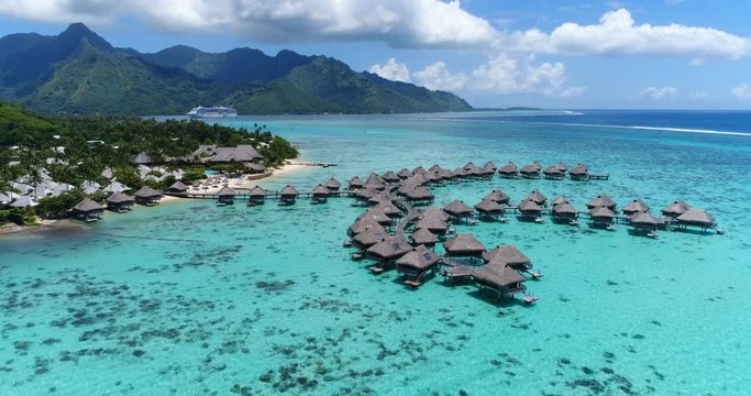 Tropical vacation paradise island with overwater bungalows resort in coral reef lagoon ocean by beach. Aerial video of Moorea, French Polynesia, Tahiti, South Pacific Ocean.