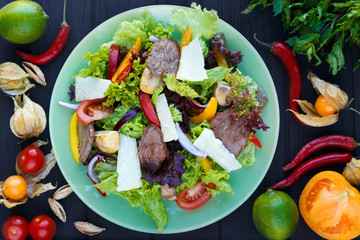 Salad with grilled veal and parmesan slices on green plate, top view