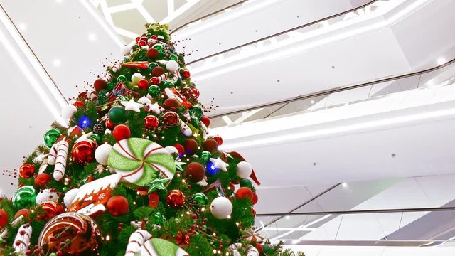 Big decorated Christmas tree in large multi-storey shopping mall flickers with festive lights.