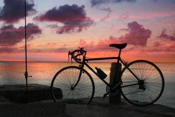 Fototapeta na wymiar Silhouette of a bike standing beside a dock by the beach with a sunset background