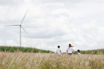 Asian family, two sons and mother running playing in field with blue sky and wind turbine in background