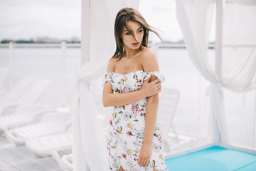 Portrait of a beautiful woman in a dress posing on a white wooden beach of summer.