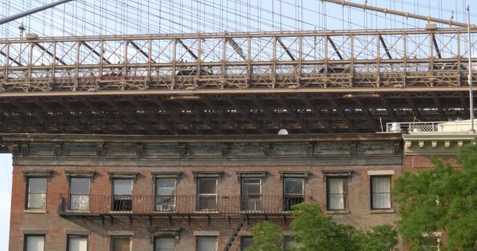 A daytime exterior establishing shot of a run down red brick apartment building under the Brooklyn Bridge. Windows with fire escapes are visible. Shot at 48fps.  	