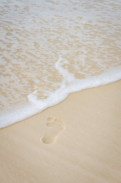 Footprint in the white soft ocean beach sands.  Waves splashing onshore.  Tourist destination location for rest and relaxation.