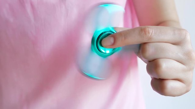 Girl playing with a glossy light colourful hand fidget spinner toy